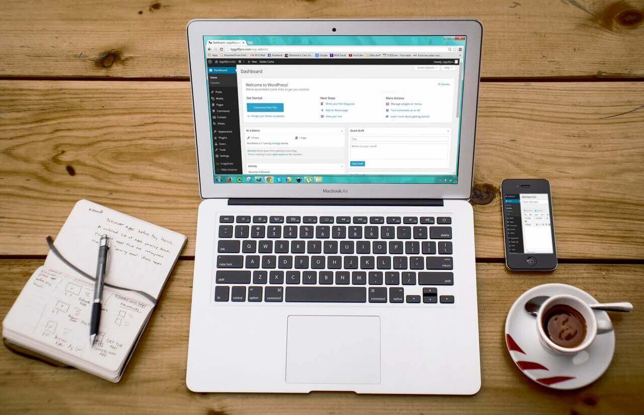 A laptop, phone, and coffee are arranged on a wooden table.
