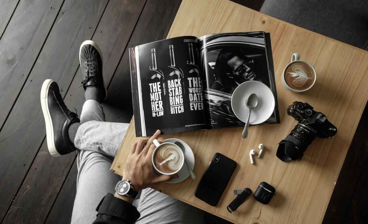 A person leisurely enjoys a cup of coffee at a table, accompanied by a book.