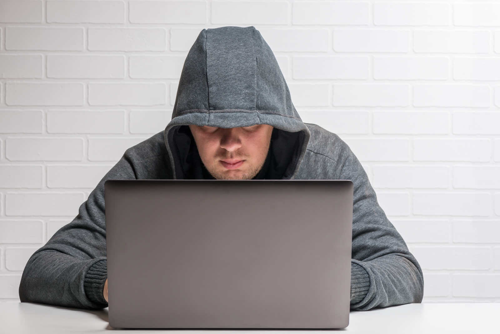 A man in a hoodie is using a laptop to blog anonymously.