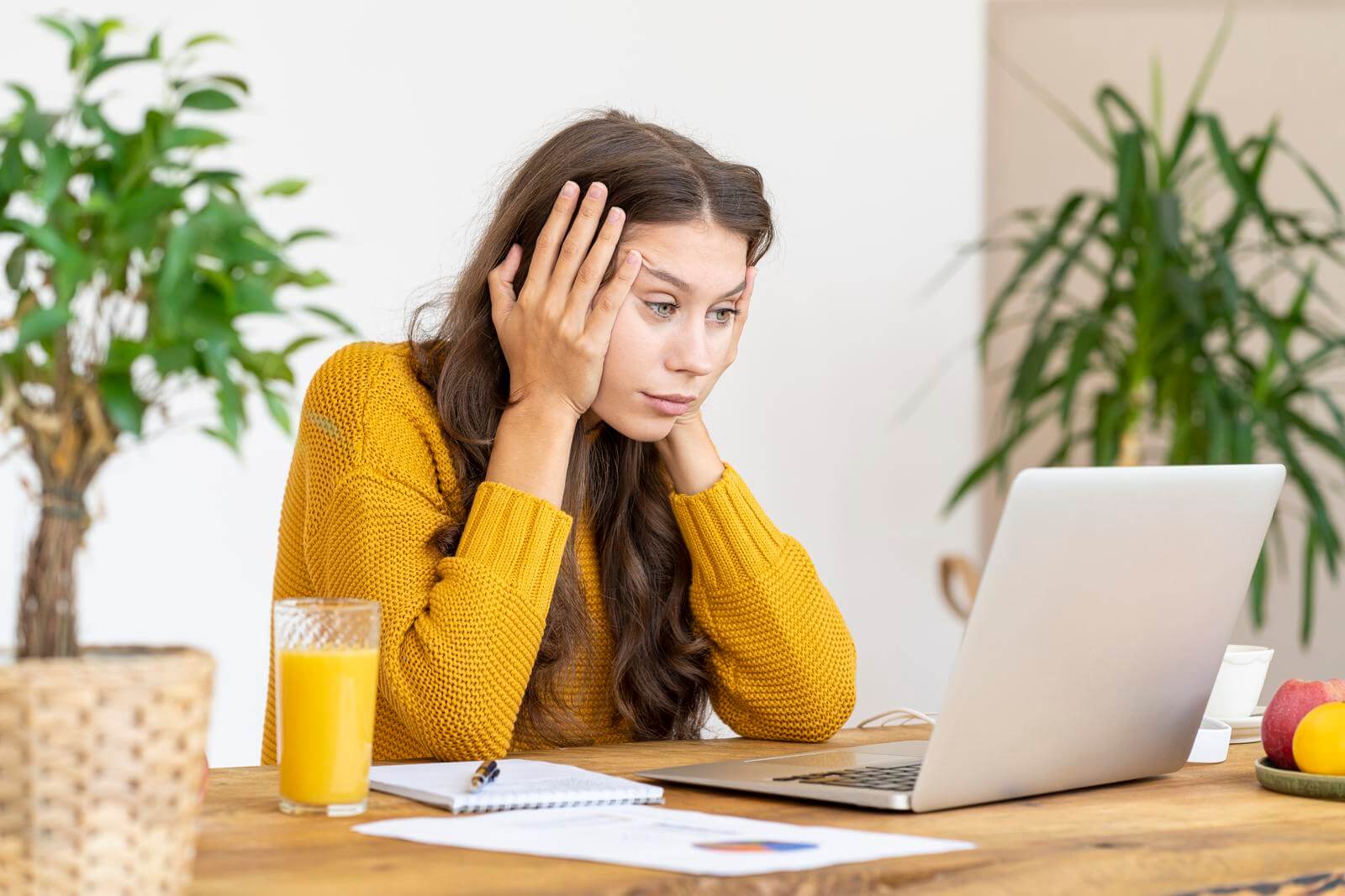 A woman is sitting at a table with a laptop in front of her, thinking of becoming a copywriter.