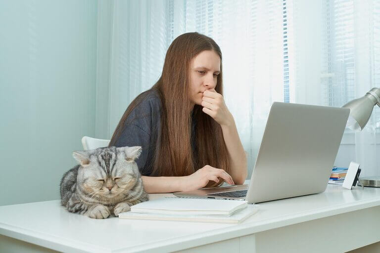 A woman multitasking at a desk, learning to be a copywriter while her cat keeps her company.