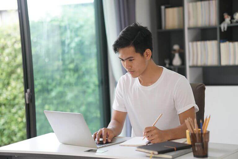 A young man is working on his laptop at home while reading the definitive guide "How Many Copywriters Are There In The World?".