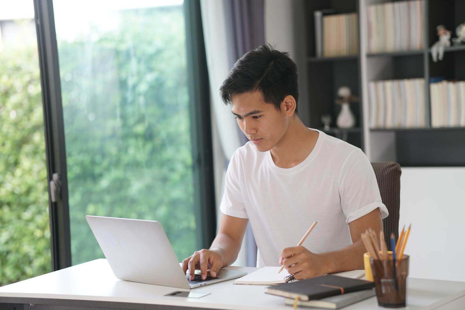 A young man is working on his laptop at home while reading the definitive guide "How Many Copywriters Are There In The World?".
