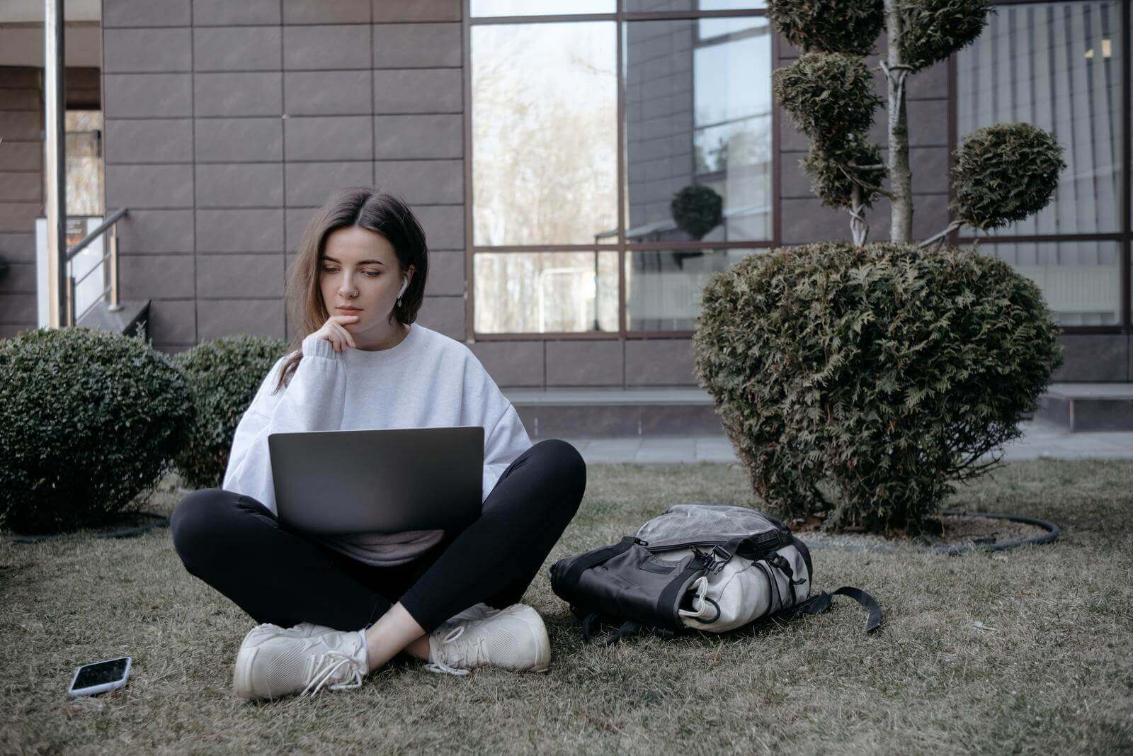 A young woman sitting on the grass with a laptop researching copywriter salaries.